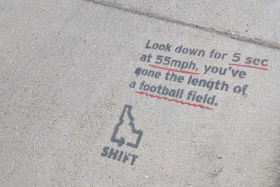 Text on a sidewalk in downtown Boise reminding drivers to pay attention: "Look down for 5 sec at 55 mph, you've gone the length of a football field."