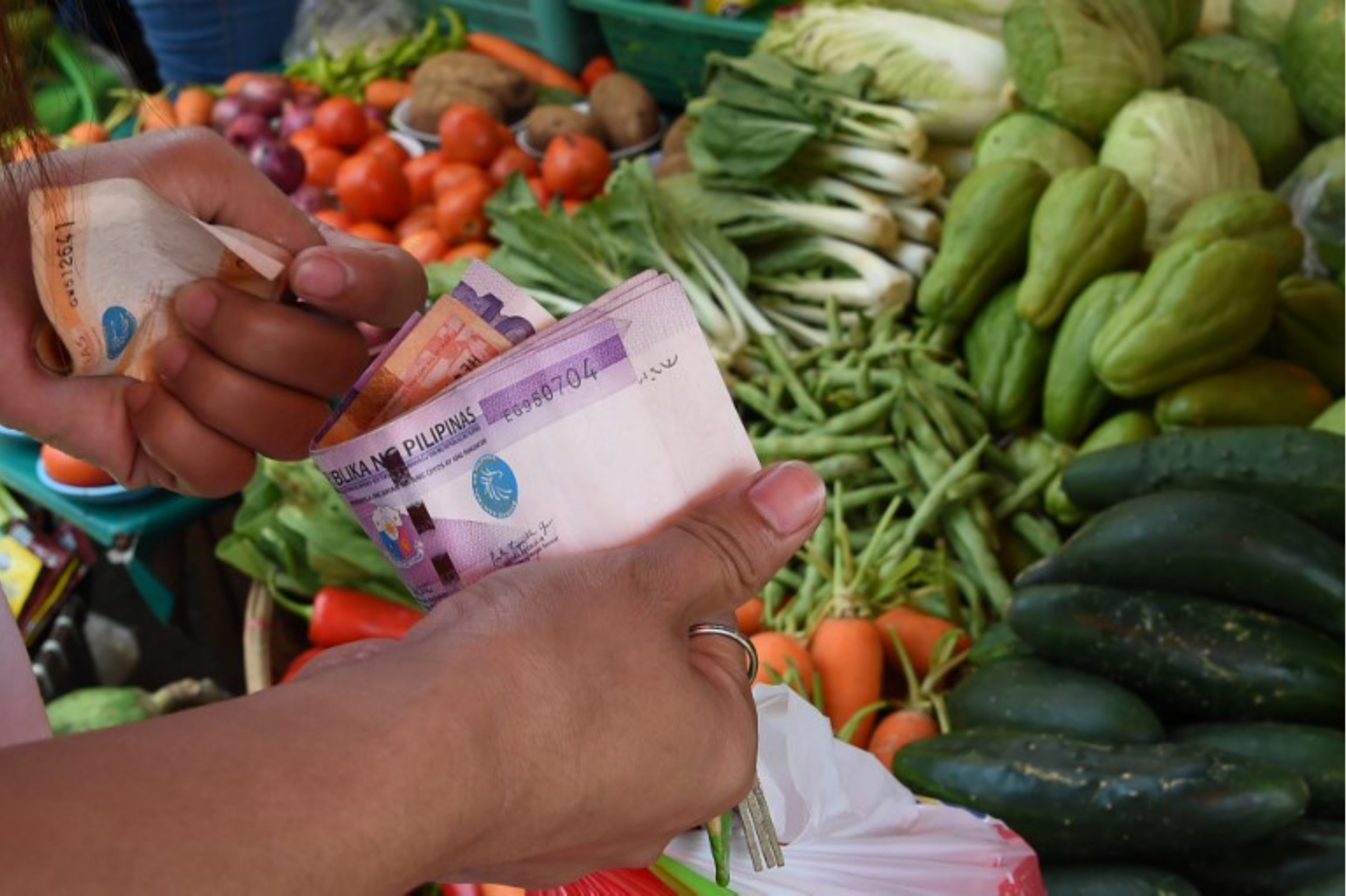 A market goer holds money in front of vegetable shelves