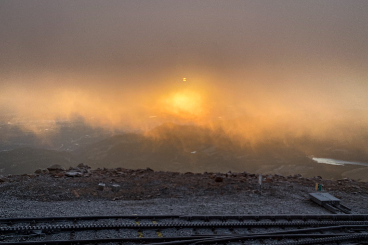 The sun rises to the east of the Pikes Peak summit with clouds casting a haze.