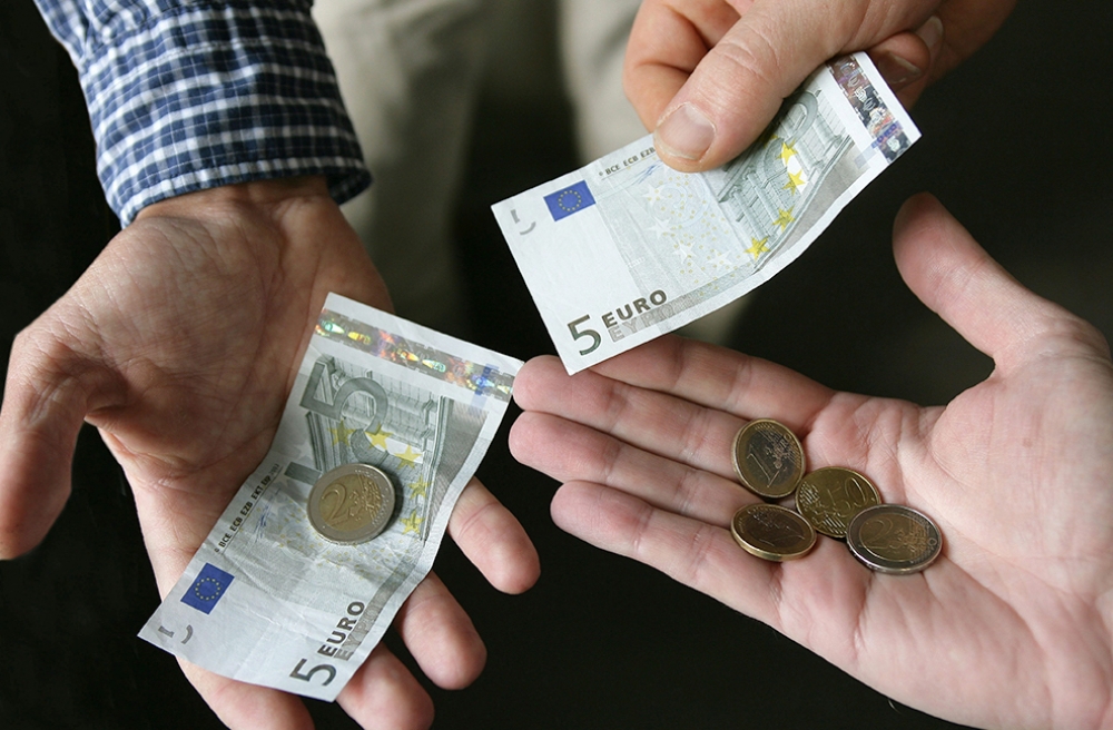 Real-term wages are falling. Image relates to minimum wage with hands holding low denomination euro notes and coins.