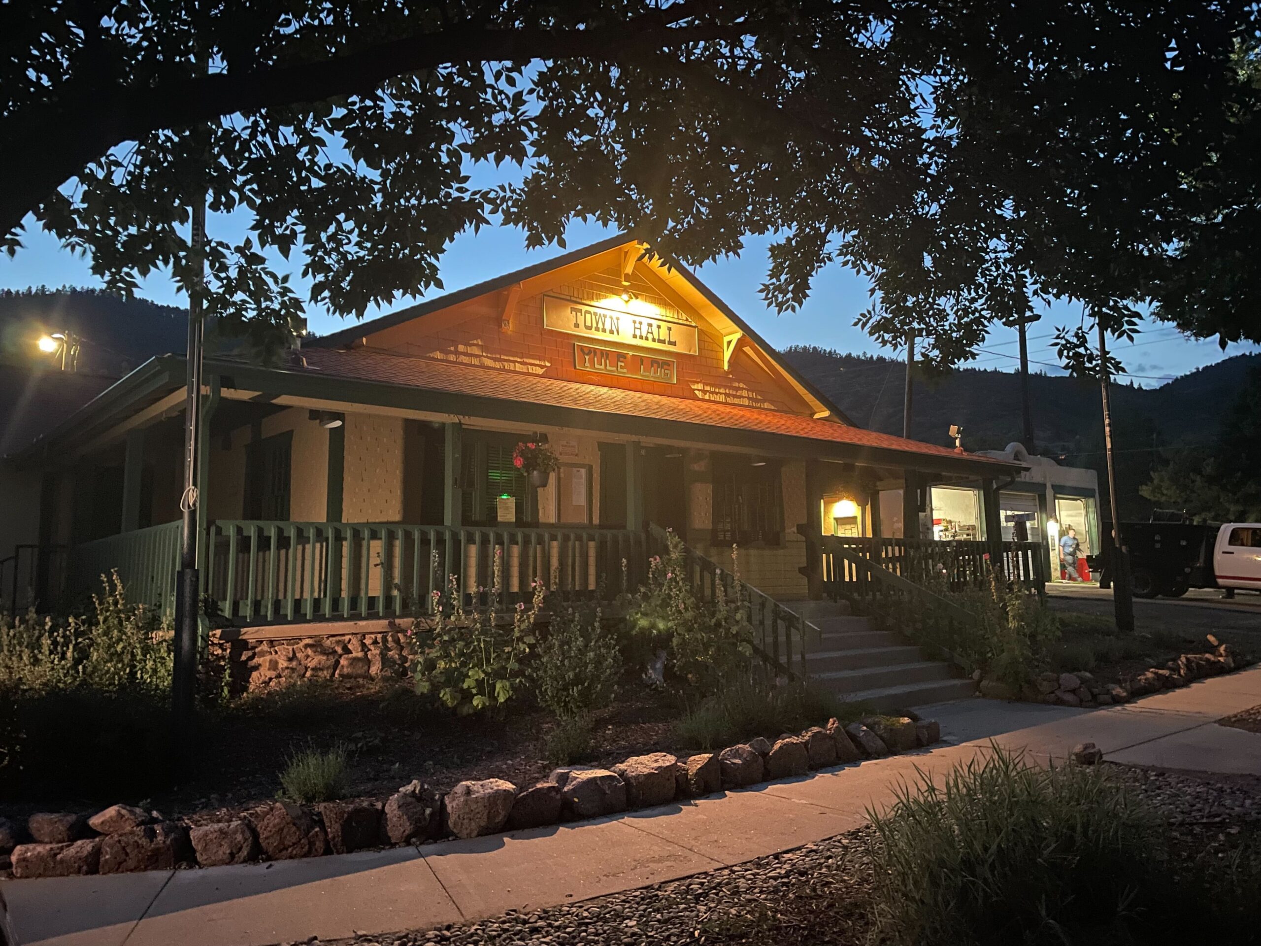 An outside shot of a single-story building with a wrap-around porch, at dusk