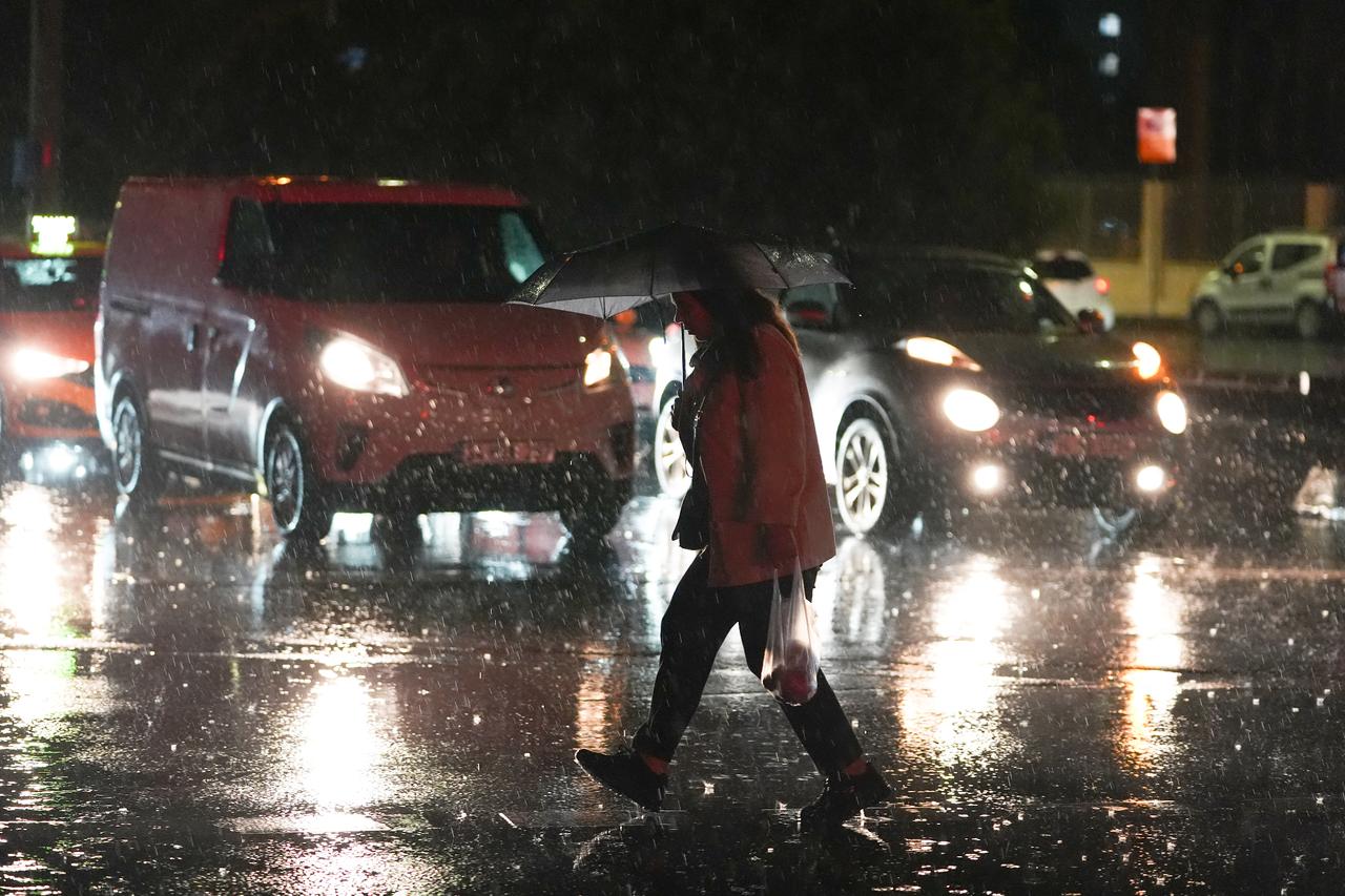 A pedestrian crosses a rain-soaked street under an umbrella as traffic slows during a heavy downpour in Istanbul, Türkiye, Oct. 27, 2025. (AA Photo)