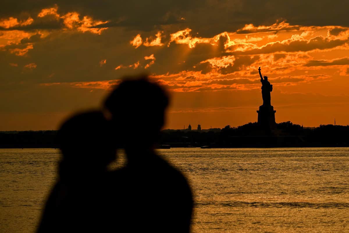 People watch as the sun sets behind the Statue of Liberty—historically a symbol of immigration to the United States—in New York, 3/7/2025 (Angela Weiss/AFP)
