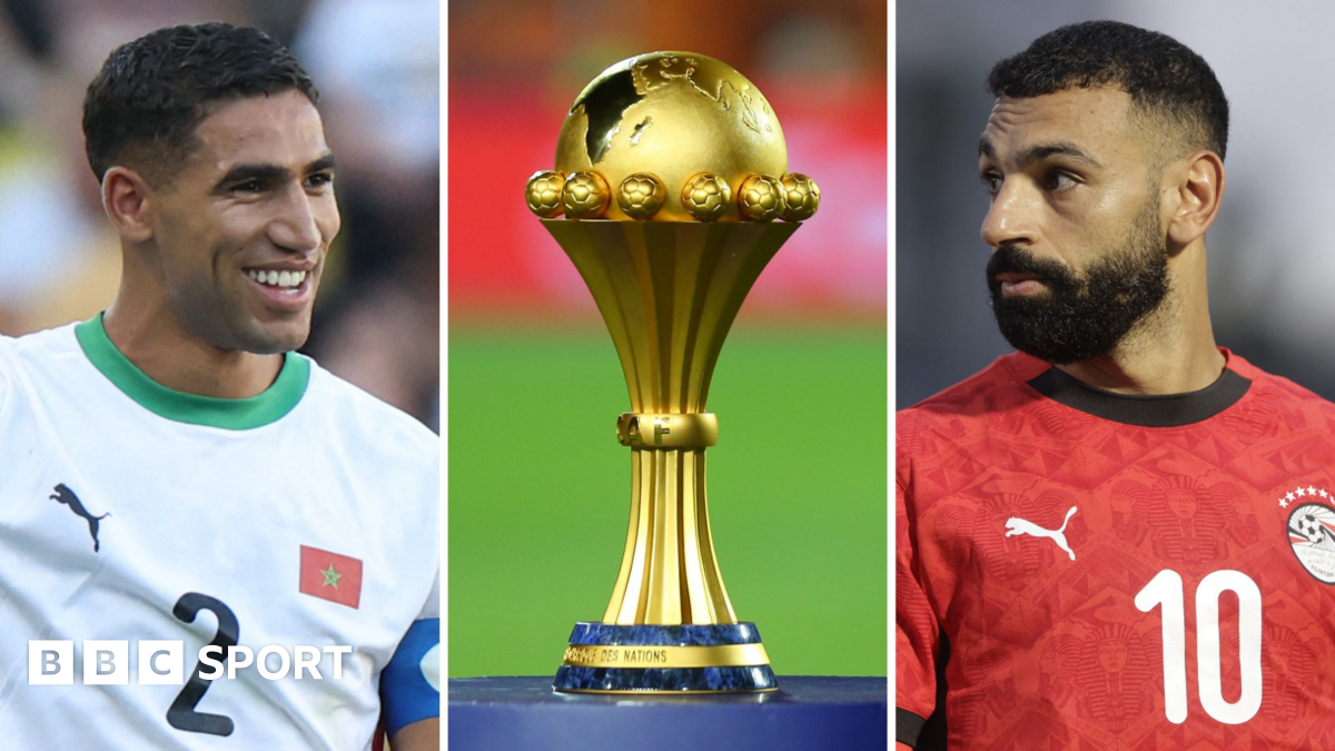 A triptych showing a vertical images of a smiling Achraf Hakimi, the Africa Cup of Nations trophy on a blue plinth and Mohamed Salah. Hakimi wears a white Morocco shirt with green trim displaying the number two on the chest, while Salah, in a red Egypt shirt bearing a number 10 on the chest, is turning his head to one side and has a serious expression on his face. Both men are visible from stomach up