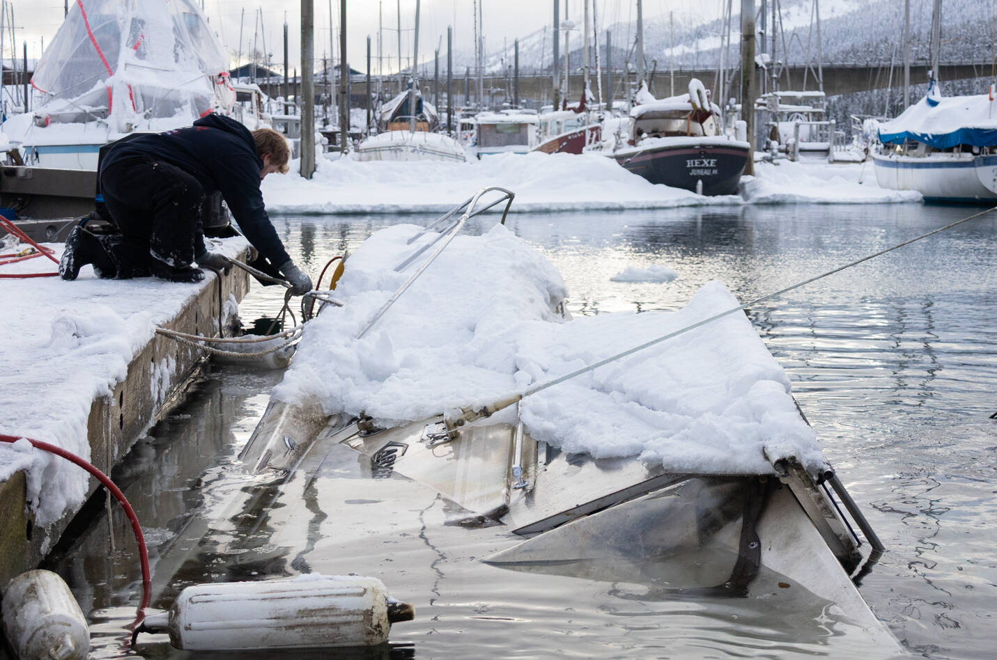 Deckhand Trevin Carlile, left, and diver Phil Sellick at Melino’s Marine Rescue refloat a sunken boat in Harris harbor on Jan. 8, 2026. Record-breaking snow at the beginning of the month caused at least eight boats to sink in Harris, Douglas and Aurora harbors, resulting in oil spills. Chloe Anderson for the Juneau Empire
