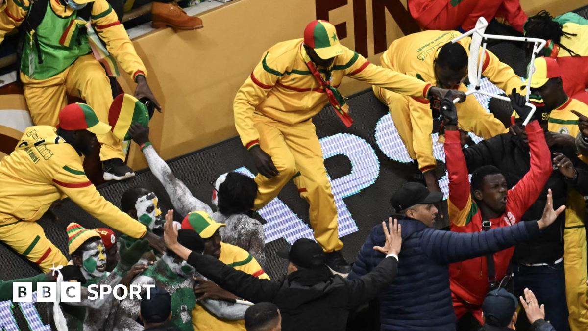Senegal fans, all dressed in yellow, green and red, are seen in a stand during the 2025 Africa Cup of Nations final. Many are shouting and gesturing down towards security staff who are standing on the edge of the playing surface looking up at them