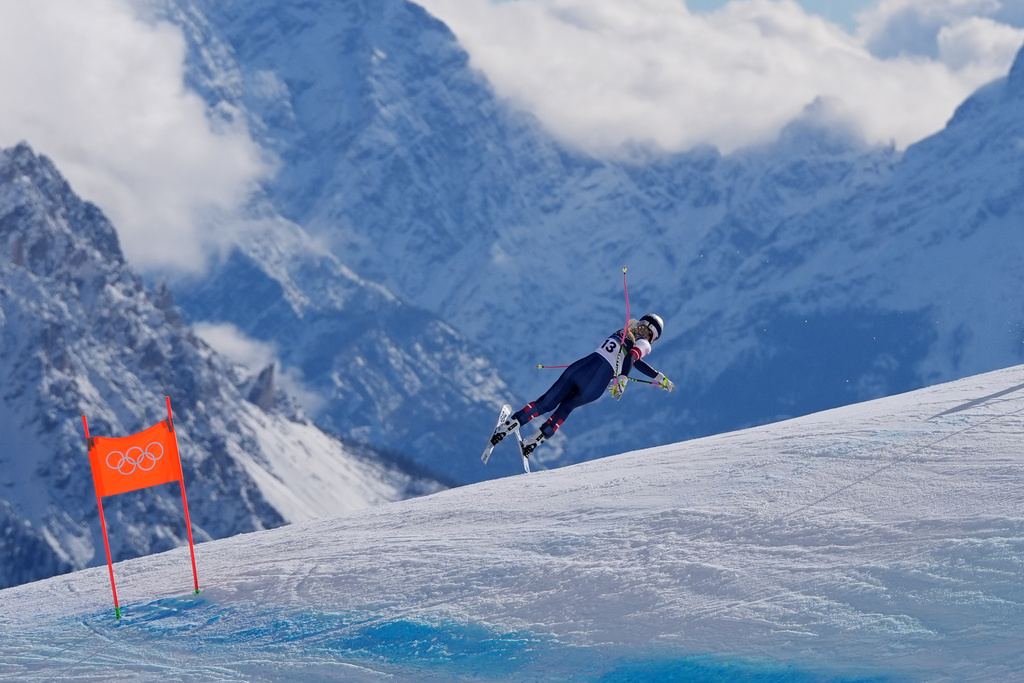 A skier crashes on a mountain with a larger mountain in the background. An orange gate is in the foreground.