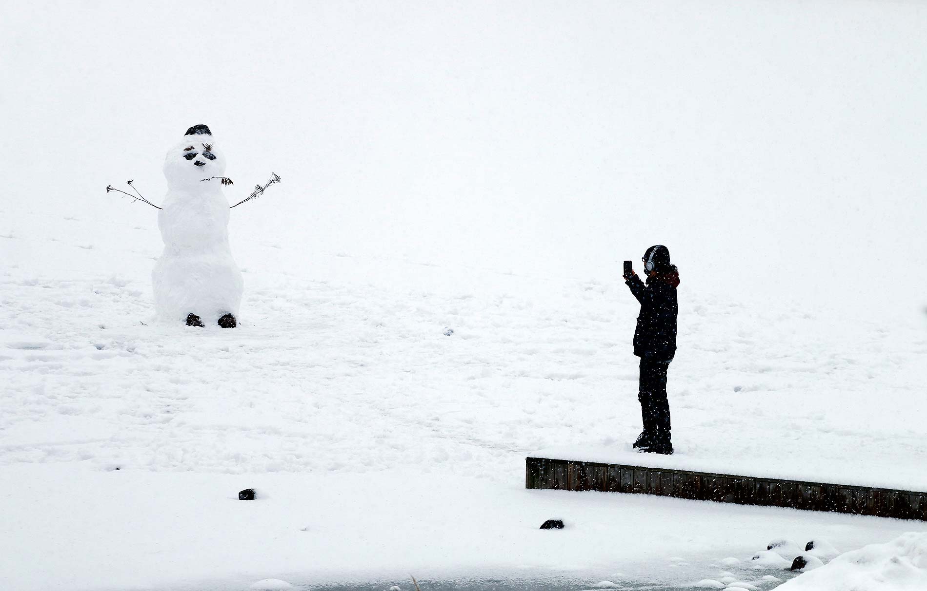 A person photographing a snowman while snow falls around them in a photo by Tony Öhberg for Finland Today.