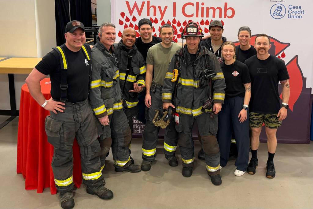 Members of the Everett Fire Department gather around battalion chief D.J. Neyens (red helmet), who is undergoing chemotherapy for multiple myeloma, as he prepares to climb the stairs to the 73rd floor of the Columbia Tower at the Blood Cancer Uniteds Firefighter Stairclimb on Sunday, March 8, 2026 in Seattle, Washington. (Aaron Coe / The Herald)