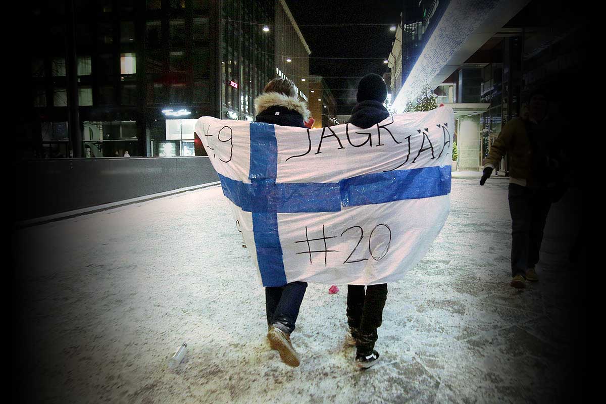 Photograph by Tony Öhberg for Finland Today showing two people walking on an icy street, each wrapped in a Finnish flag over their shoulders.