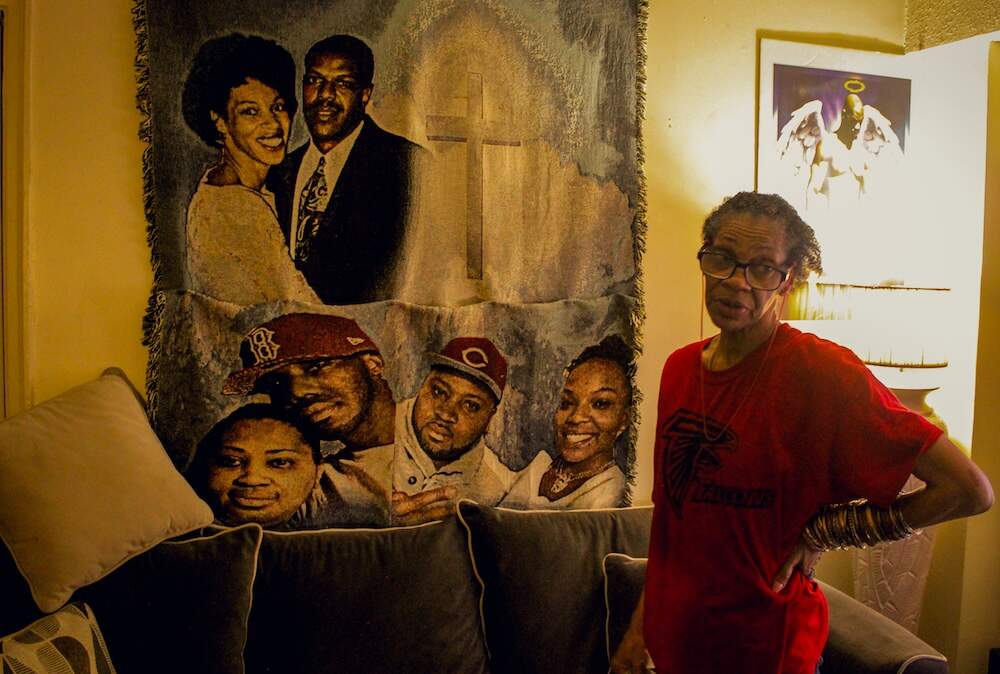 A tapestry hangs inside Michelle Thomas's Springfield living room, displaying her family and children beside a cross. Glowing above Thomas is an image to remember her son, Carl Sepheus Jr., who was killed in 2018. (Julia Goujiamanis for WBUR)