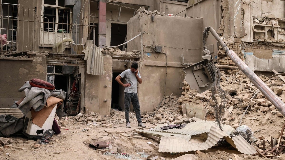 A man speaks on a mobile phone as he stands outside damaged homes, following a military strike on the Iranian capital Tehran on March 15, 2026.