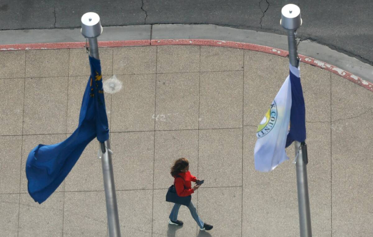 A pedestrian walks along Third Street as wind blows flags on Monday, March 2, 2026, in Las Vega ...