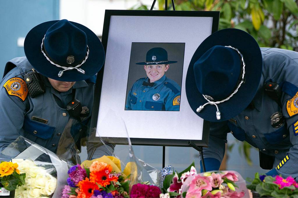 Two troopers place a photo of slain Washington State Patrol trooper Chris Gadd outside WSP District 7 Headquarters about twelve hours after Gadd was struck and killed in a collision on southbound I-5 about a mile from the headquarters in March 2024 in Marysville. (Ryan Berry / The Herald)