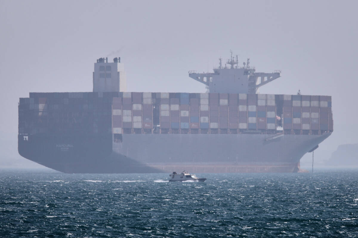 A container ship sits at anchor as a small motorboat passes in the foreground in the Strait of ...