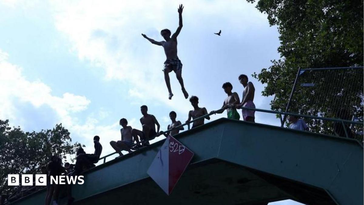 A person jumps off a bridge into the Canal Saint-Martin as public swimming having been allowed earlier on part of it due to rising of temperatures