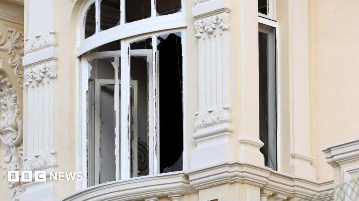 Close up of a largely blown out window, with small shards of glass around its border, in a light-yellow building in Monaco. It is the site of the explosion in which three people were injured on Monday evening.