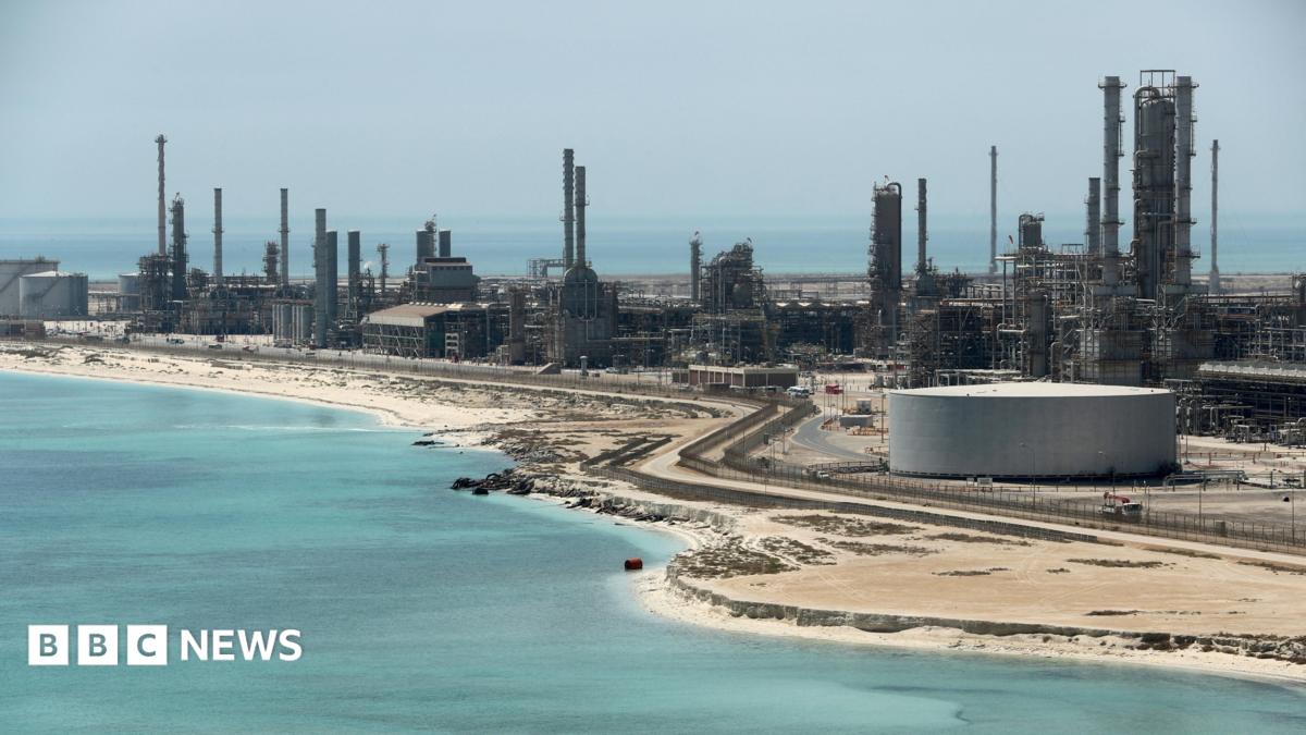 A file photo of Aramco's Ras Tanura oil refinery and oil terminal, which lies along a stretch of coast. The site comprises a network of several tall chimney-shaped structures and smaller buildings. It is daytime and the water along the coastline is a clear blue.