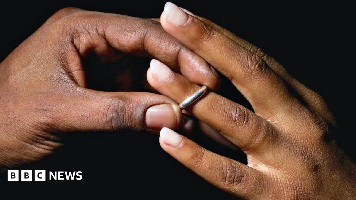 A man places a silver wedding band onto a young woman's ring finger.