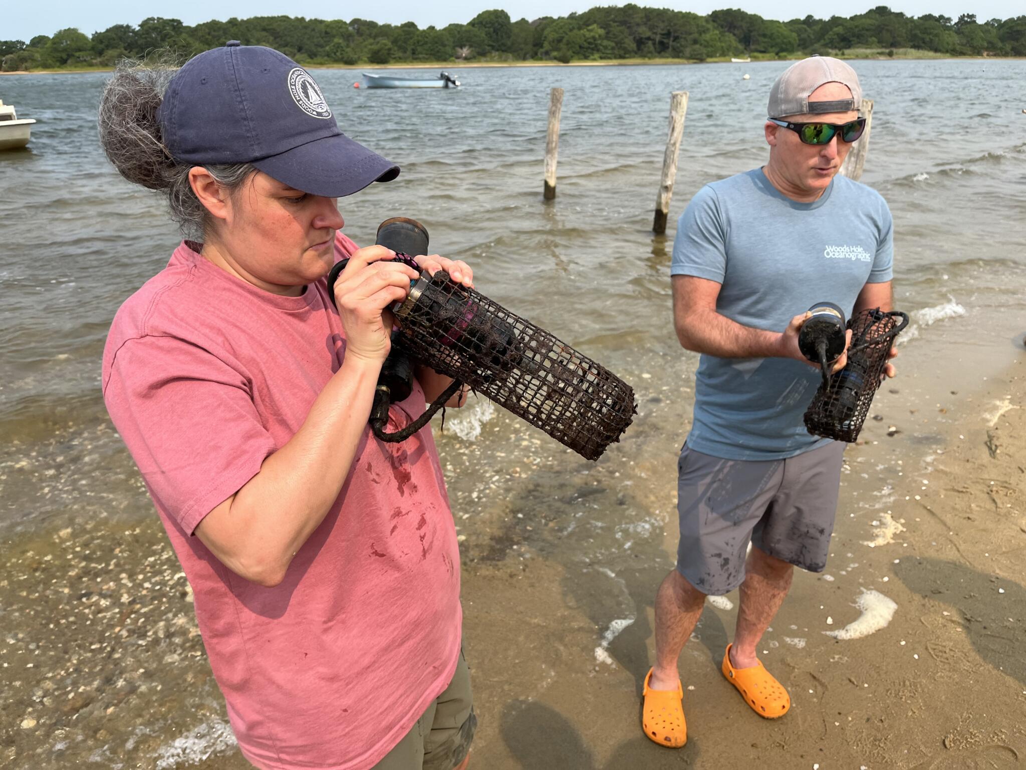 WHOI Research Associate Andria Salas and Senior Scientist Aran Mooney inspect underwater recording devices called SoundTraps after retrieving them from Tisbury Great Pond on Martha’s Vineyard. July 15, 2026 (Barbara Moran/WBUR)