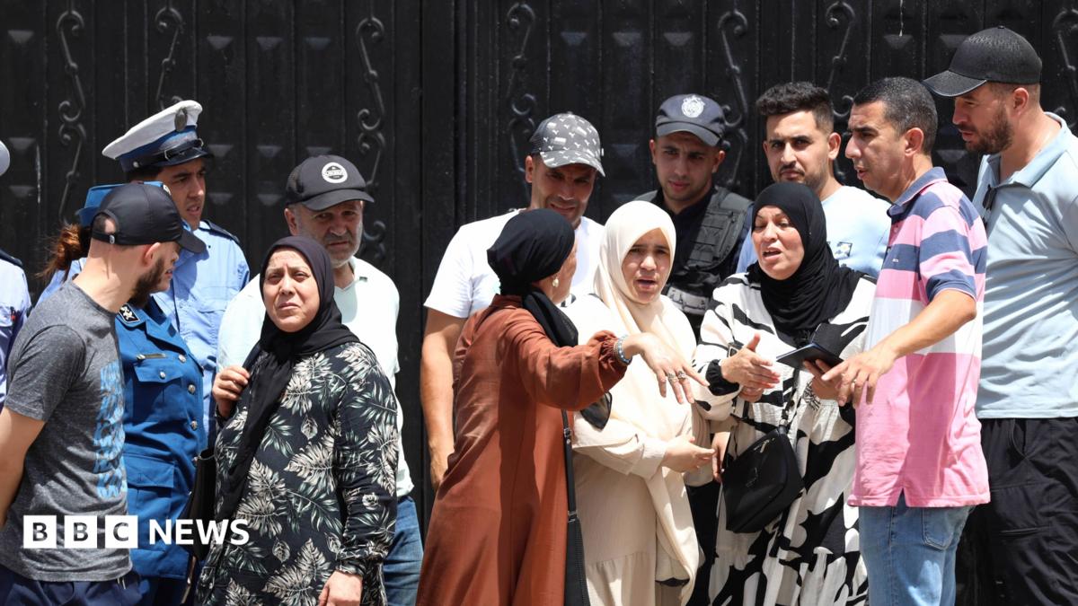 Police stand guard at a black gates of an orphanage in Algiers as a crowd of men and women gesticulate outside