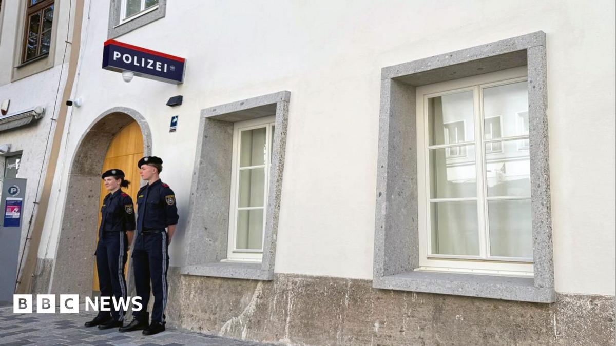 Two police officers stand outside a white-washed building with a police sign in German on the wall