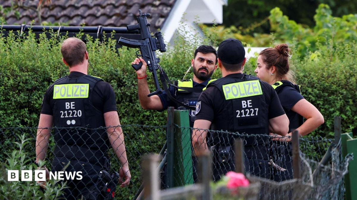 Four police officers are pictured, with one officers holding a gun up