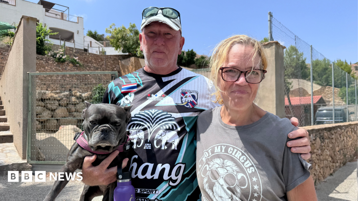 A man, holding a dig and wearing a Thai sports shirt with Chang beer as a sponsor, puts his arm round a woman wearing an olive green T-Shirt