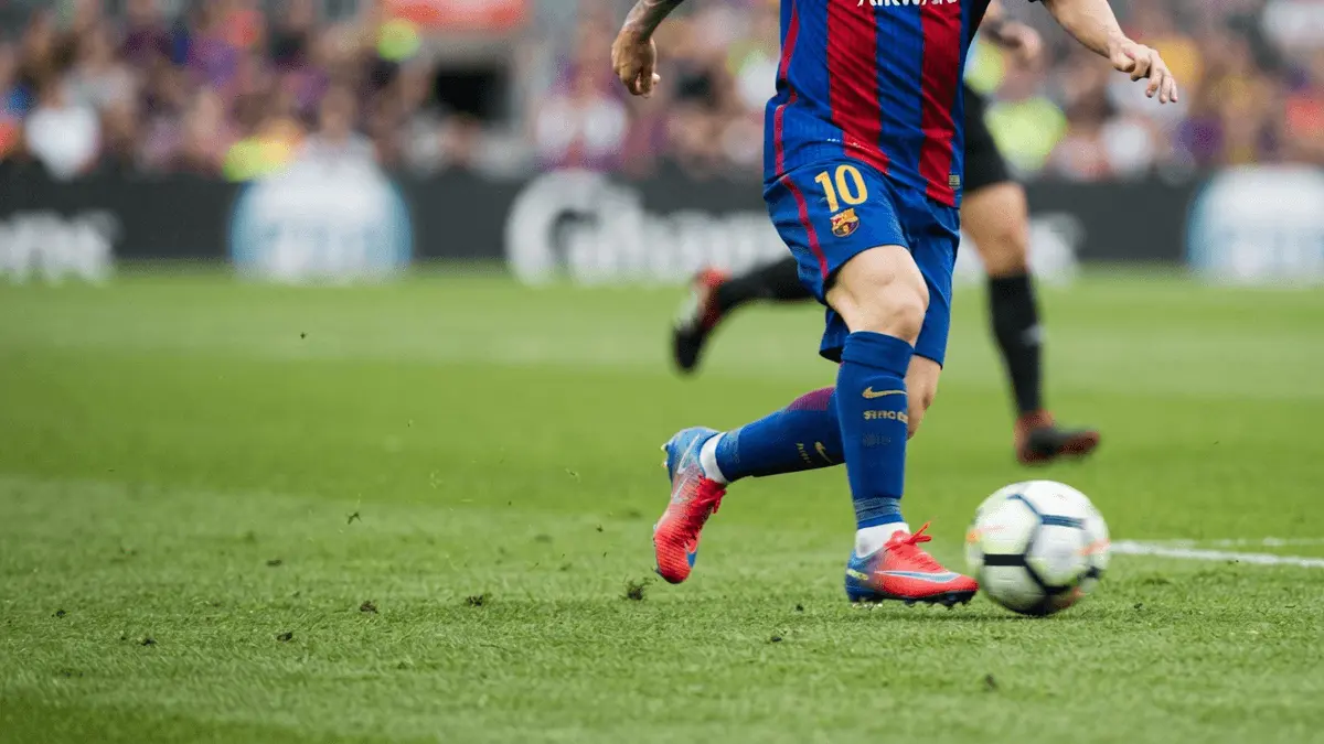 Barcelona player dribbling on right wing in blue and red kit on grass pitch