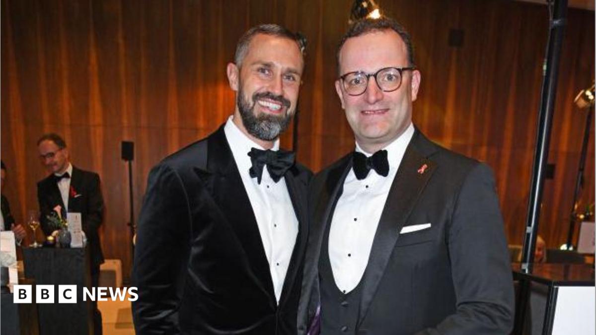 Jens Spahn (R) in glasses, a grey jacket and white shirt and bowtie beside his husband Daniel Funke who has as beard and a black velvet jacket with a white shirt and bowtie