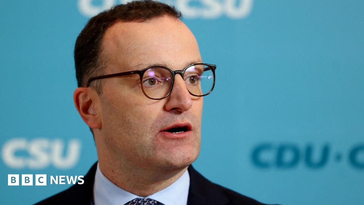Jens Spahn speaks with German media during a party meeting, he is wearing a black suit and black glasses.