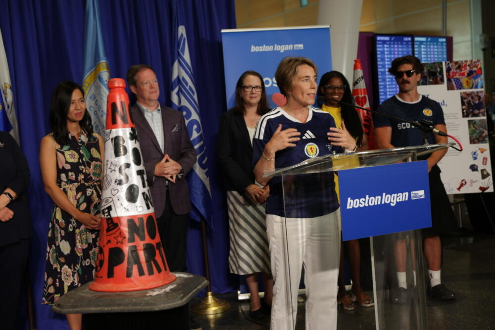 Boston Mayor Michelle Wu and a host of Massachusetts and Scottish officials look on as Massachusetts Gov. Maura Healey lauds a traffic cone at Logan Airport (Robin Lubbock/WBUR)
