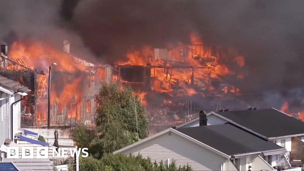 Several houses on fire engulfed in dark smoke, with untouched houses in front of them