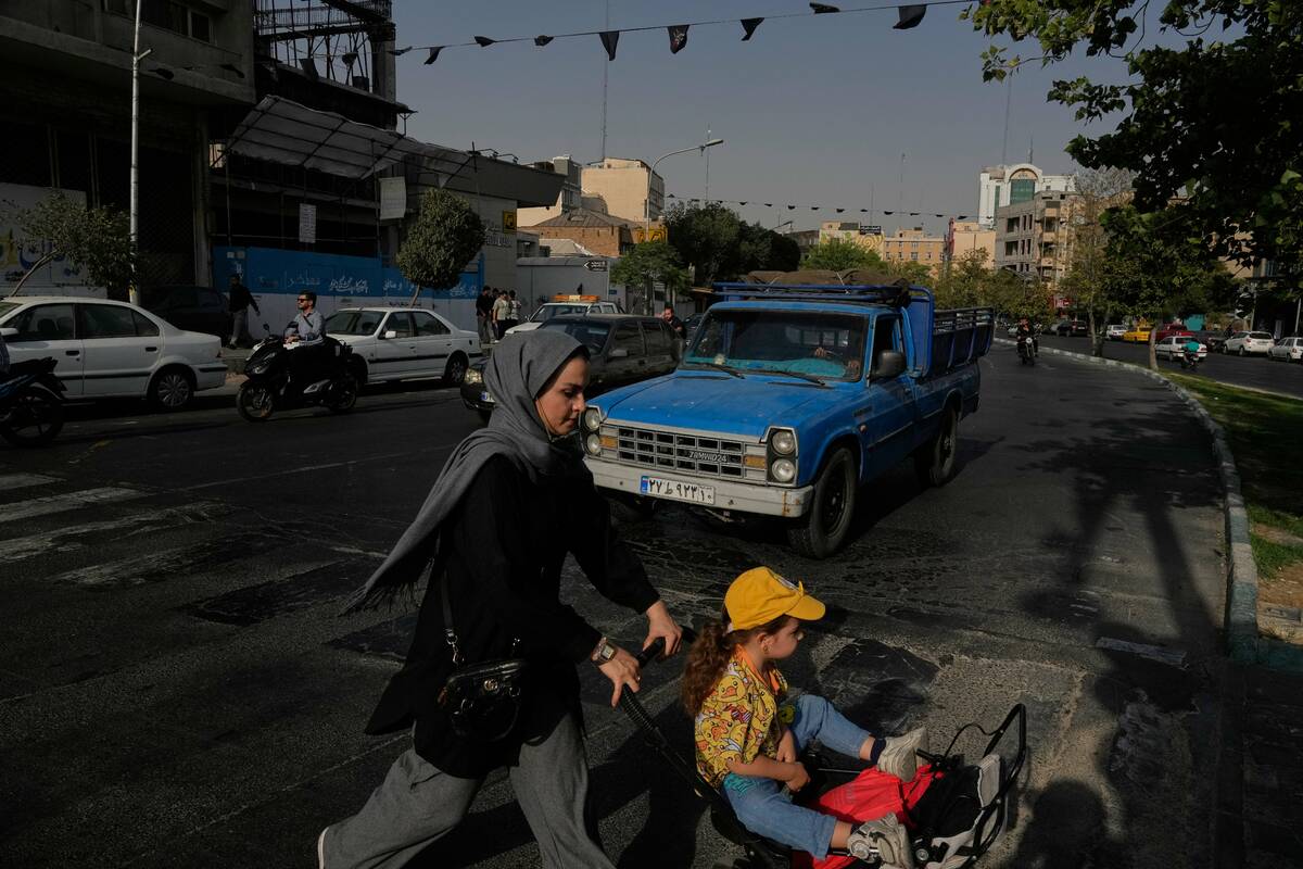A woman crosses a street with a girl in downtown Tehran, Iran, Wednesday, July 22, 2026. (AP Ph ...