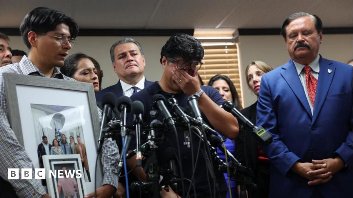 A man holds his hands over his eyes as he stands before a bank of microphones and a man holding up pictures of Lorenzo Salgado Araujo