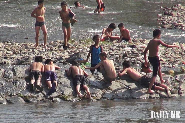 Boys swim and rest along a rocky riverbank on the Yalu River near Hyesan, Ryanggang province