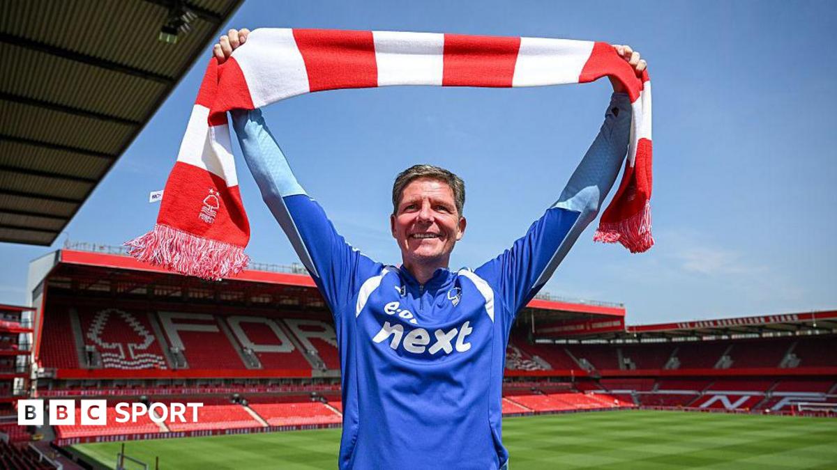 Oliver Glasner faces into the sunshine holding a red and white bar scarf, with the City Ground pitch and stands in the background