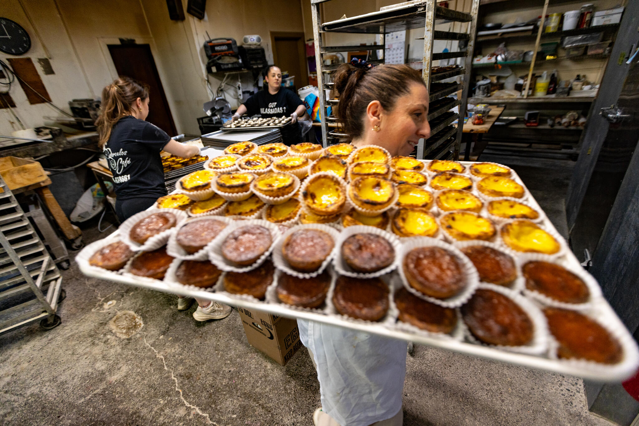 Sara Rodrigues carries a sheet pan of pasteis de nata, or creamy custard cups, for service at Barcelo’s Bakery in Fall River. (Jesse Costa/WBUR)