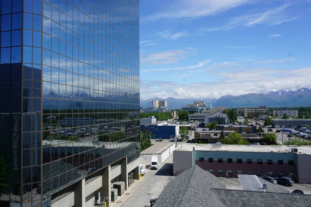 Part of the Anchorage skyline is reflected in the south-facing windows of downtown’s Robert B. Atwood Building on June 17, 2026. Anchorage, Alaska’s biggest city, had a cost of living that was 25.5% above the national urban average in 2025, according to the Alaska Department of Labor and Worforce Development. (Photo by Yereth Rosen/Alaska Beacon)
