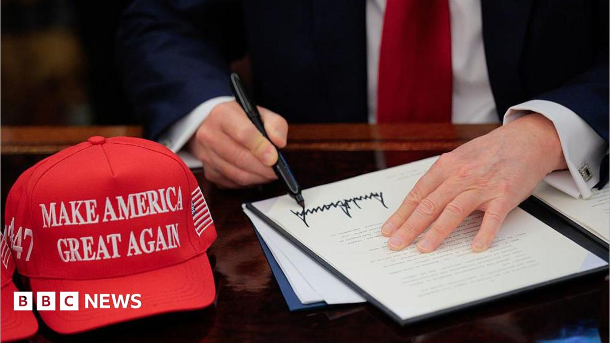 US President Donald Trump signs an executive order in the Oval Office at the White House in Washington, DC on 23 April 2025.  A red baseball hat embroidered with "Make America Great Again" in white thread sits to the left of the document, which shows Trump's distinctive signature