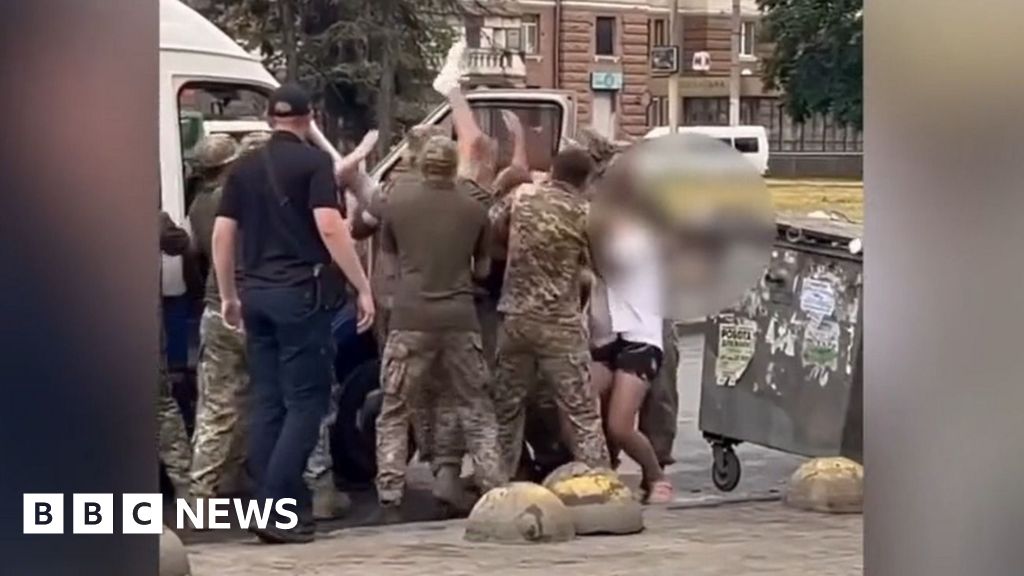 A group of men in army uniforms carrying a man into a van