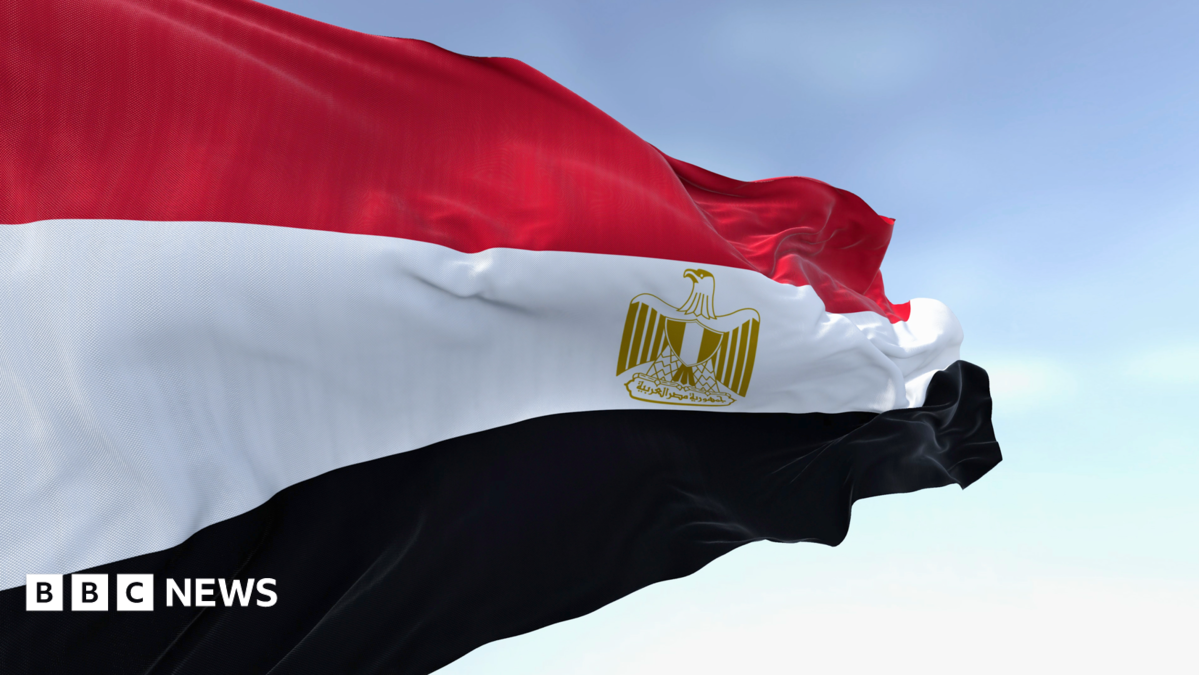 Close-up of the Egypt national flag waving. A clear blue sky is in the background.