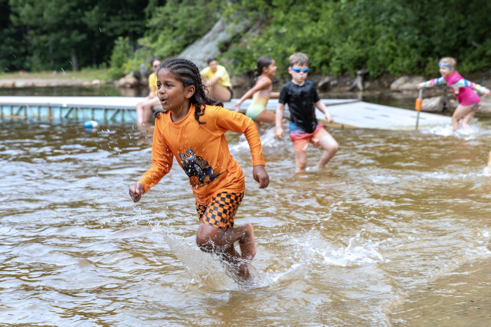 Campers run through the shallow water in the swimming area at Hale Education's day camp in Westwood. (Robin Lubbock/WBUR)