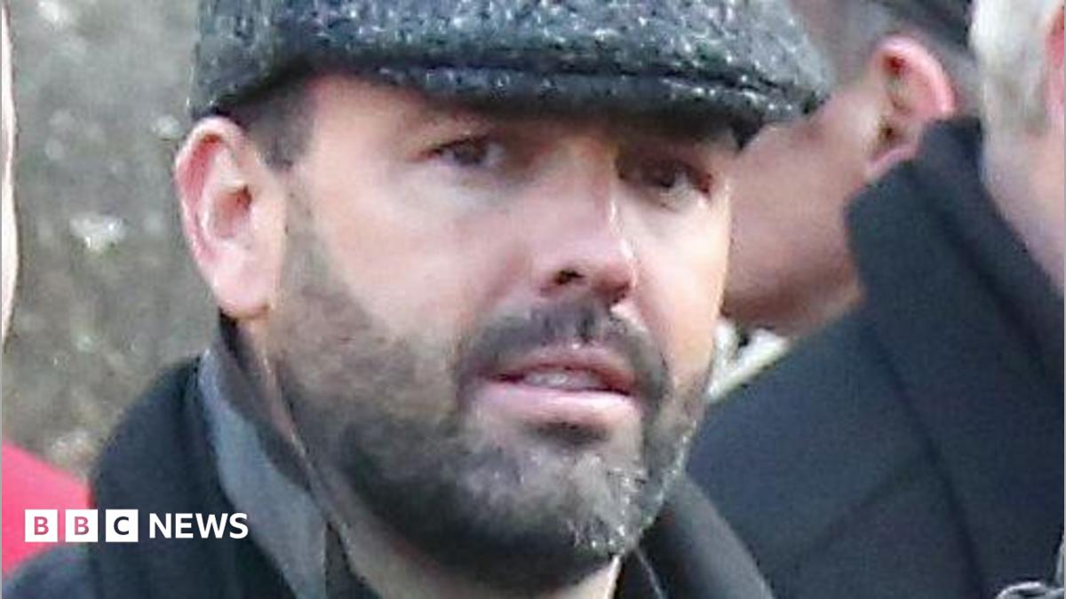Daniel Kinahan, a man with short dark hair and a stubbly beard, pictured at a funeral in 2016.  He is wearing a grey peaked cap, a black shirt and a black coat with the collar pulled up.