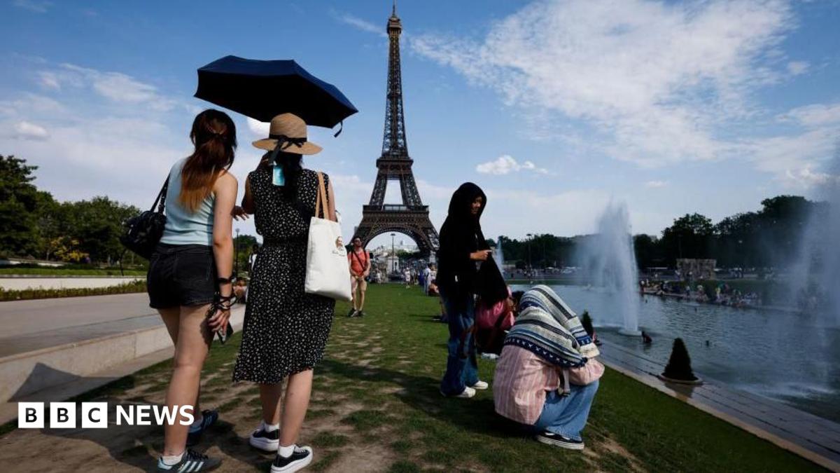 Women shelter from the heat under a black umbrella at the Trocadero Fountain by the Eiffel Tower, in Paris, France, 20 June 2026. Other people are seated next to the river.