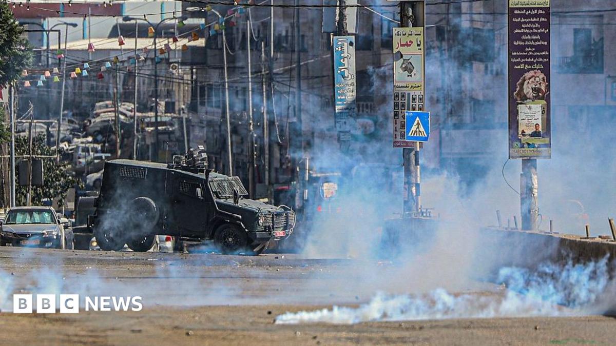 An Israeli armoured vehicle moves along a street as tear gas fills the air, during a raid in Qalandia refugee camp, in the occupied West Bank (25 August 2026)