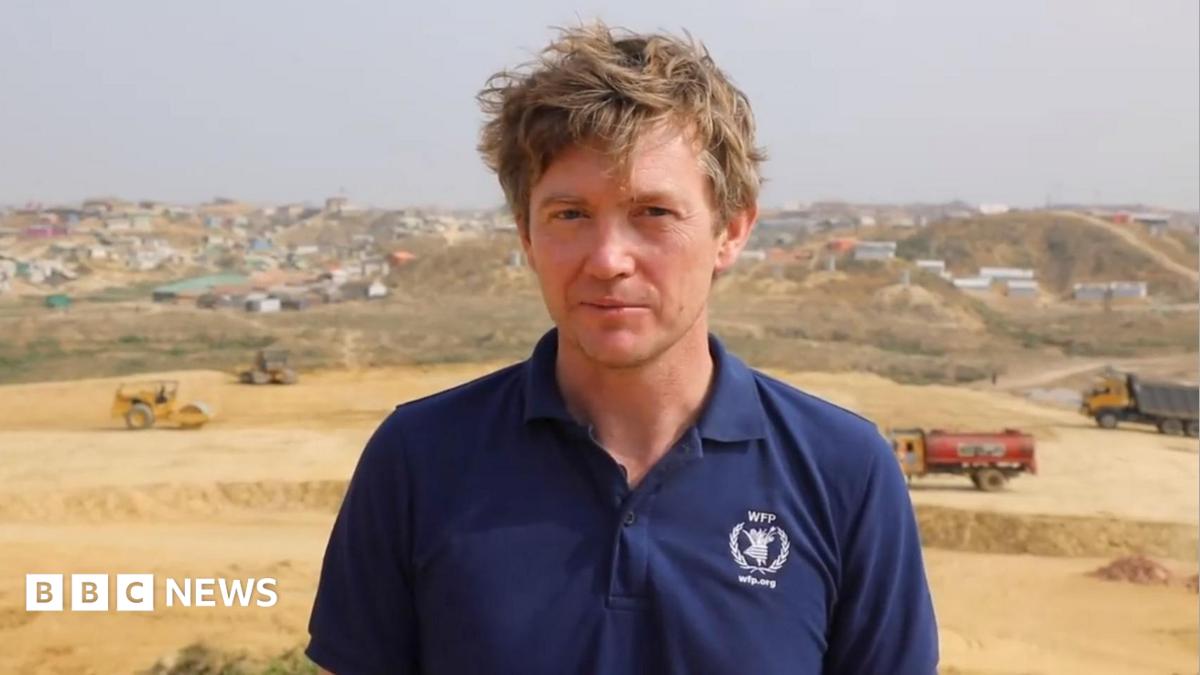 A man with brown hair looking at the camera, he is wearing a navy polo top