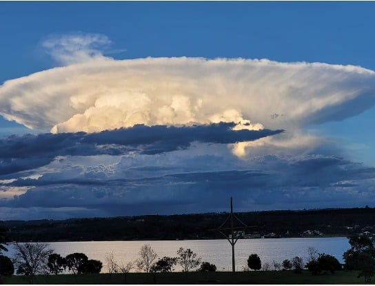 A towering anvil-topped thunderstorm cloud over water, the kind of severe cell driving the Brazil bomb cyclone red alert in Rio Grande do Sul.