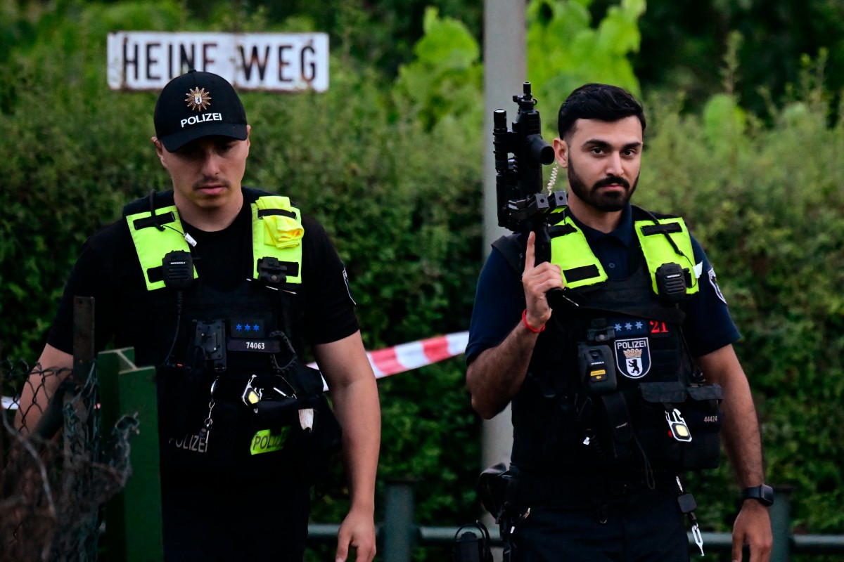 Police officers walk with automatic weapons in an allotment complex in the western Spandau district of Berlin on July 26, 2026, in a garden area near the scene where the chief suspect in the previous nights' deadly attack near Berlin's Pride parade has been shot dead. German police searched on July 26, 2026 for a suspect believed linked to Islamist circles after a car ploughed into a crowd near Berlin's Gay Pride celebrations, killing one person and wounding 16 others. The incident shattered what had been a day of celebration for hundreds of thousands attending Christopher Street Day, one of Europe's largest Pride events, and left revellers fleeing a central Berlin park as sirens echoed through the night. (Photo by John MACDOUGALL / AFP)