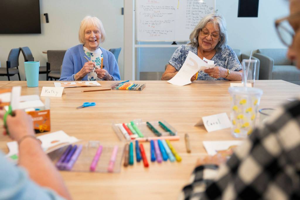 Kathy Hoppenrath and Judy Deeter chat while cutting out their dog coloring art during Old Friends Club at the Lynnwood Neighborhood Center on Wednesday, Aug. 12, 2026 in Lynnwood, Washington. (Olivia Vanni / The Herald)